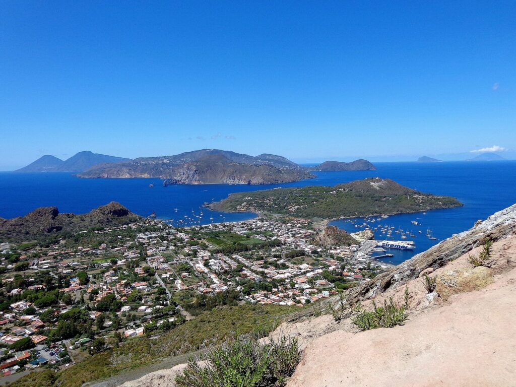 Il mare di Lipari con vento: come scegliere la costa — Ascensione al Gran Cratere (386), Panorama. Sullo sfondo al centro l'isola di Lipari, Vulcanello, la spiaggia le Sabbie Nere a nord e Sabbie