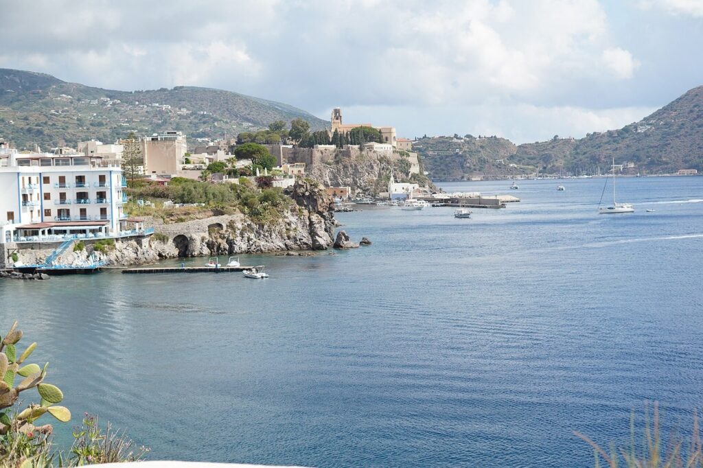 Dove dormire a Lipari senza noleggiare un mezzo — The castle and harbour of Lipari seen across the bay from the seafront terrace of the Hotel Carasco, in the Aeolian Islands, Sicily, Italy.