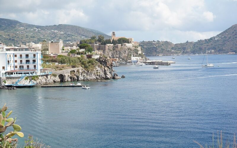 Dove dormire a Lipari senza noleggiare un mezzo — The castle and harbour of Lipari seen across the bay from the seafront terrace of the Hotel Carasco, in the Aeolian Islands, Sicily, Italy.